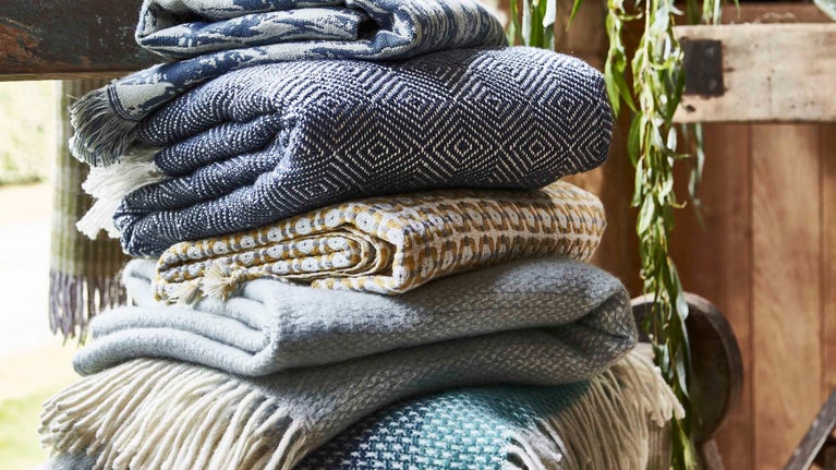 A pile of National Trust blanket throws displayed on a wooden table